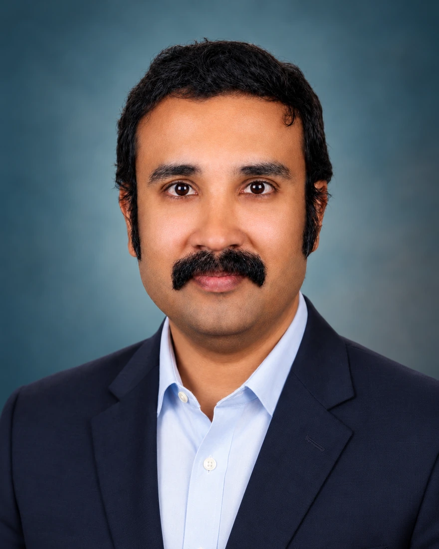 Dr Joe M Das, consultant neurosurgeon, in a navy suit against a muted teal studio background